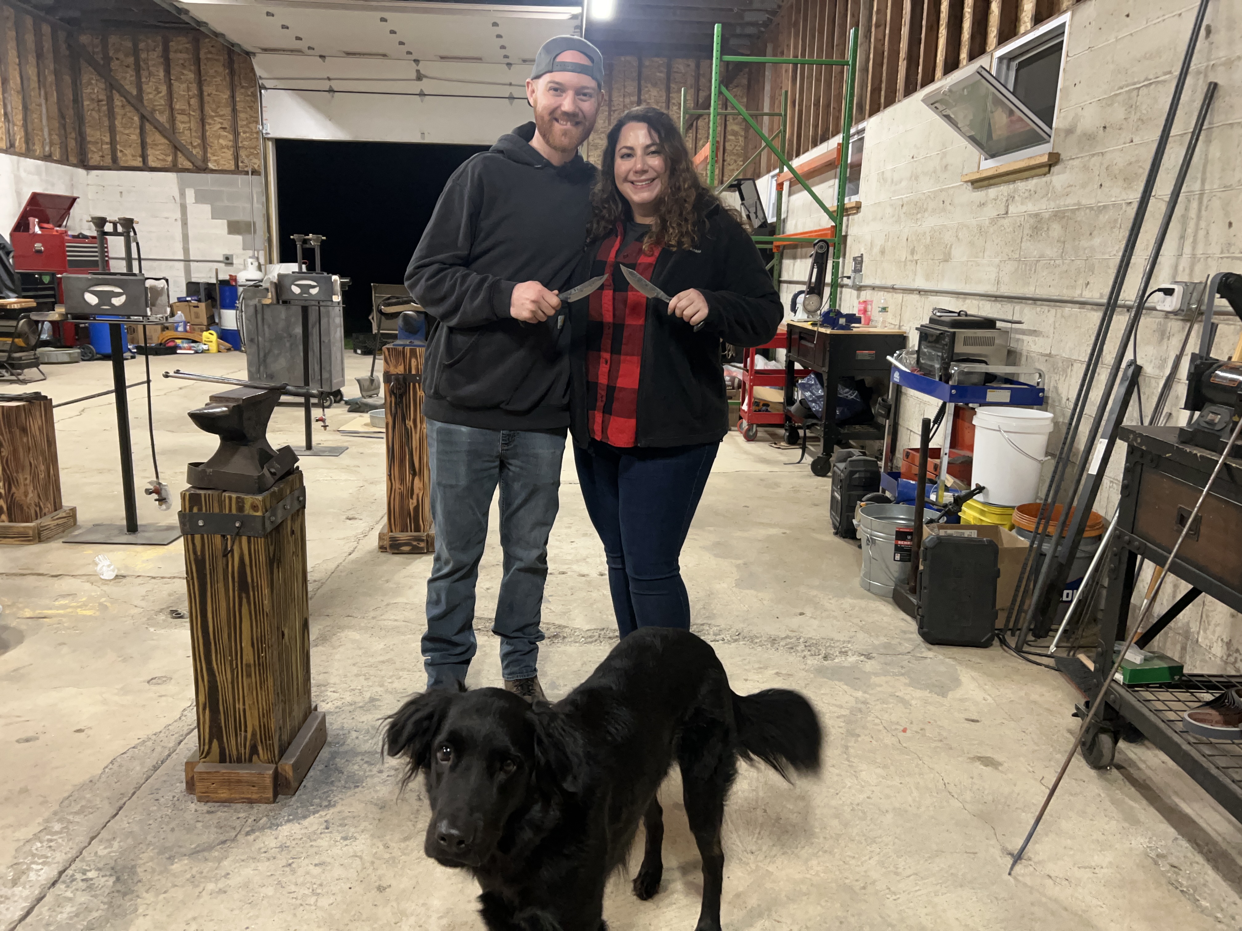 A couple forging glowing steel together at an anvil in a blacksmith shop